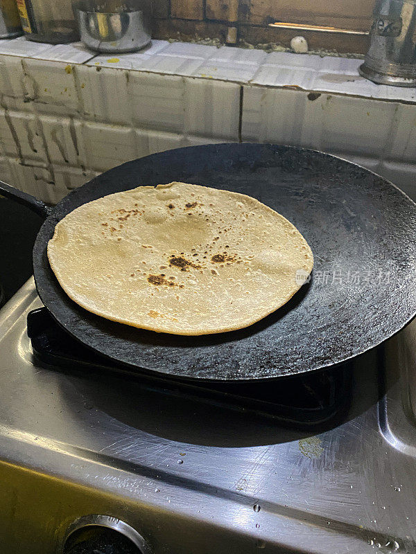 roti / chapatti在铸铁tawa(扁平，圆形的烹饪锅)上烹饪的图像，厨房炉子燃气燃烧器，全麦atta面粉，高架视图，重点在前景